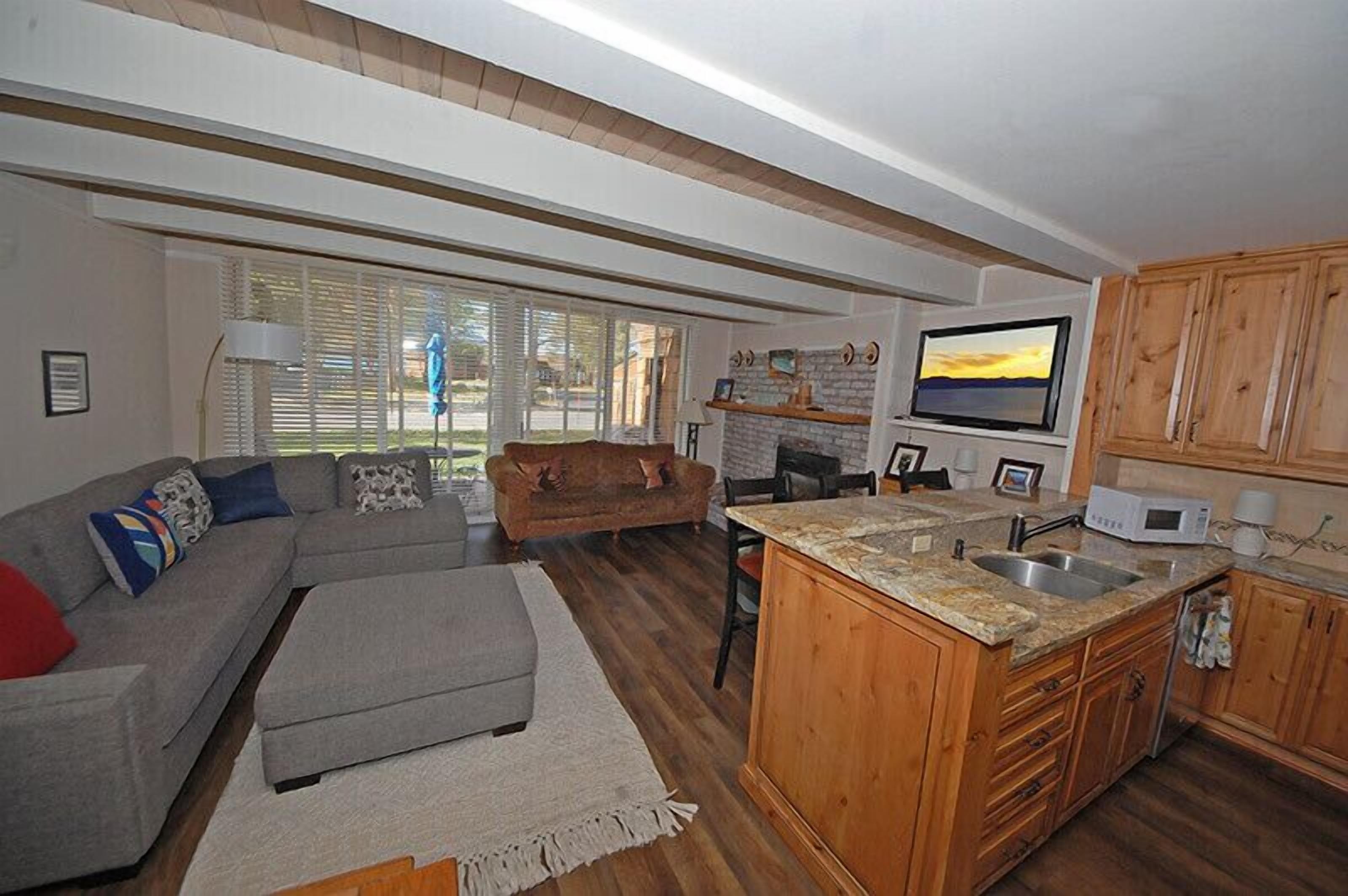 Ein gemütlicher Wohnbereich mit Sofa, Hocker, Küchenzeile mit Holzschränken und Fernseher.