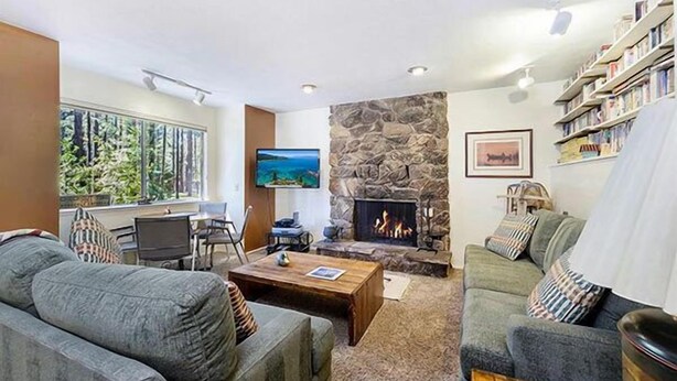 A cozy living room with a stone fireplace, comfortable seating, a television, and a bookshelf.