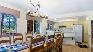 A dining area with a wooden table and chairs, a chandelier, and a view of the outdoors through large windows.