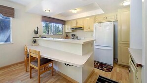 A modern kitchen with a central island, wooden chairs, and a refrigerator.