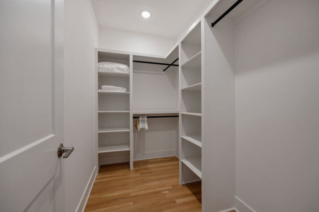 Ein begehbarer Kleiderschrank mit weißen Regalen und Holzboden.