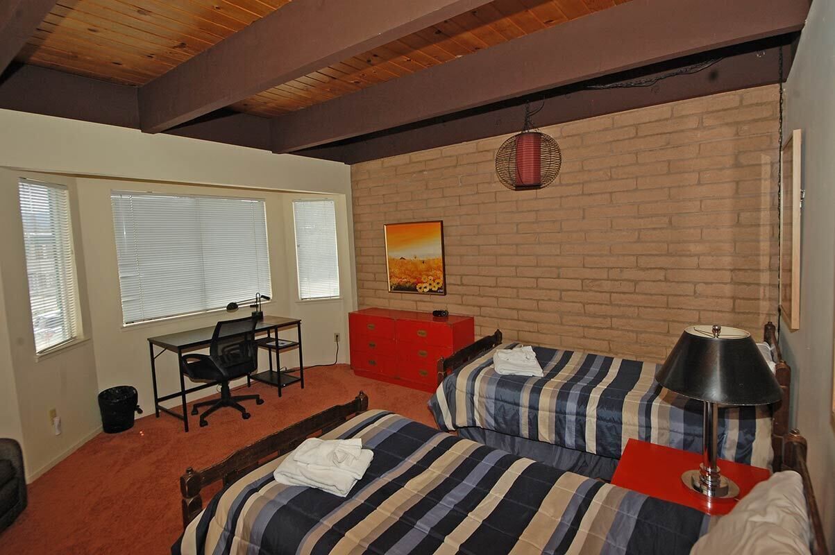 A bedroom with a brick wall, a desk, a computer, a bed with striped bedding, and a red dresser.