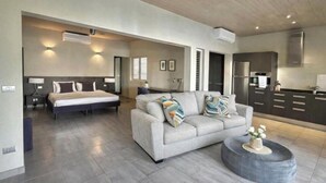 A modern living room with a sofa, a bed, and a kitchen area. - Stunning Waterfront Suite, Antigua English Harbour (English Harbour)