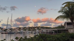 A marina with boats docked, a building with a covered area, and a palm tree. - Stunning Waterfront Suite, Antigua English Harbour (English Harbour)