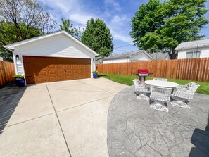 A backyard with a concrete patio, a wooden fence, a barbecue grill, and a white garage. - Cute & cozy family-friendly Royal Oak ranch close to downtown and highways! (Royal Oak)