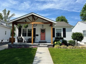 Een gelijkvloers huis met een overdekte veranda, een voordeur en een kleine tuin.