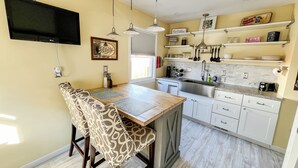A compact kitchen with a dining area, featuring a wooden table, patterned chairs, a built-in sink, and white cabinetry. - Cute & cozy family-friendly Royal Oak ranch close to downtown and highways! (Royal Oak)