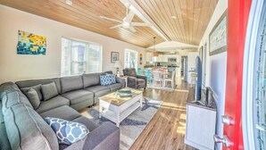 A spacious living room with a grey sectional sofa, a wooden ceiling, and a red door.