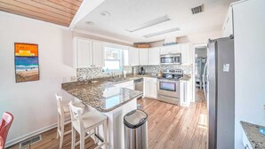 A modern kitchen with white cabinets, granite countertops, stainless steel appliances, and a wooden ceiling.