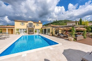 Une piscine avec un espace patio, un bâtiment à deux étages doté de balcons, et une colline en arrière-plan.