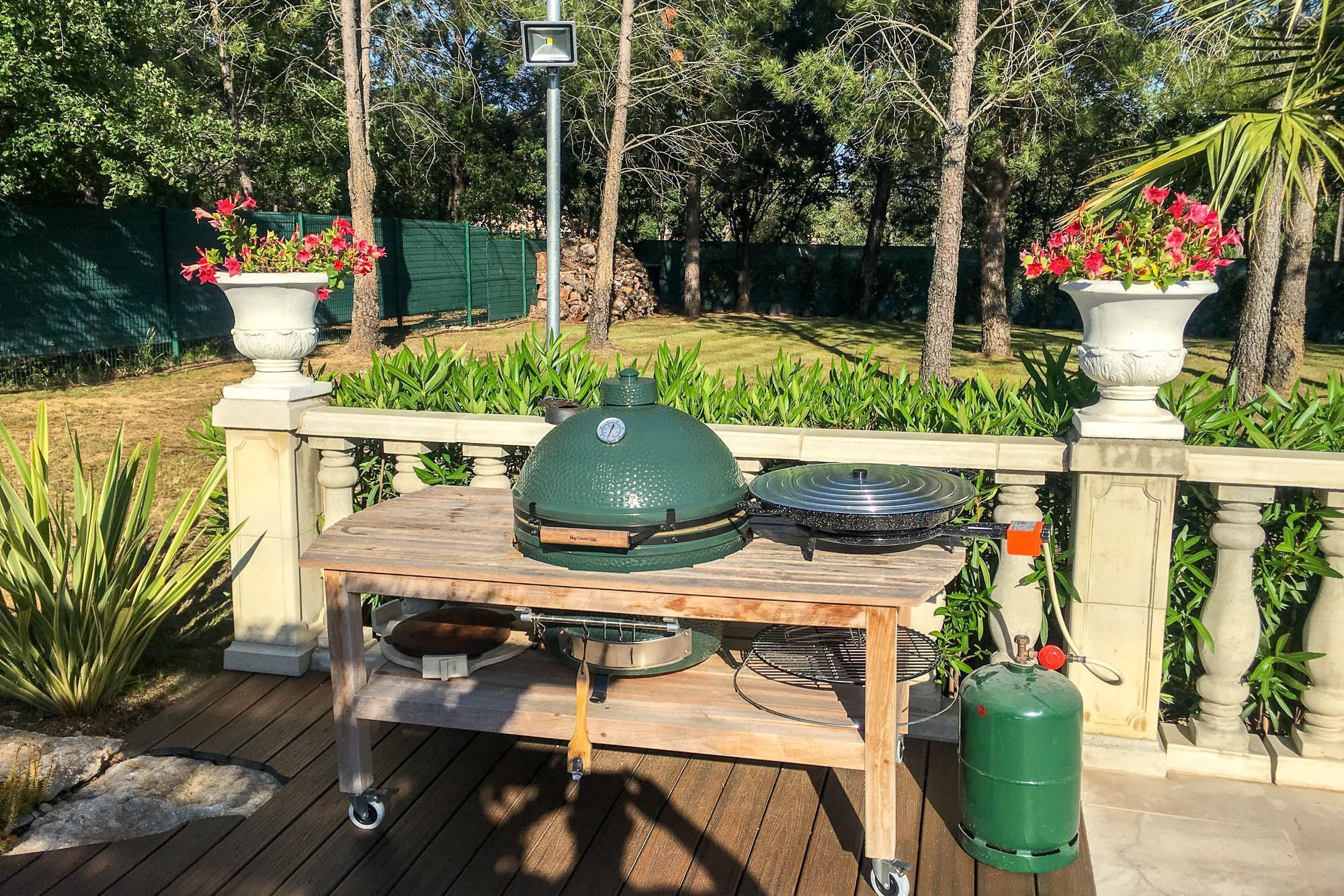Un barbecue portatif install é sur une table en bois munie de roulettes, avec une bouteille de gaz et un thermomètre.