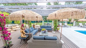 Une terrasse extérieure avec des meubles en osier, une piscine et des parasols en chaume.