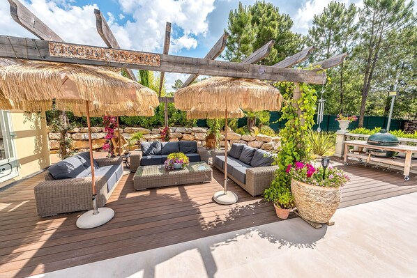 An outdoor patio with wicker furniture, thatched umbrellas, and potted plants.