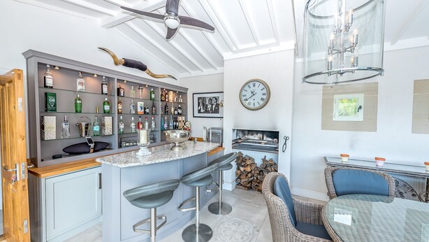 Une cuisine moderne dotée d’un coin bar, de tabourets de bar, d’un ventilateur de plafond, d’une horloge et d’une cheminée.