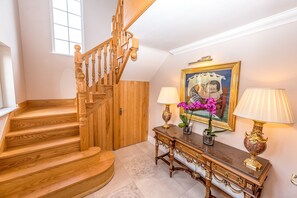 Un escalier en bois menant à un palier où se trouvent une console, deux lampes et un tableau encadré.
