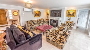 A living room with a fireplace, patterned sofas, a red ottoman, and a television.