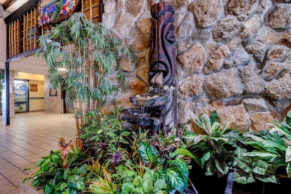 A stone wall with a decorative wooden carving, indoor plants, and a tiled floor.