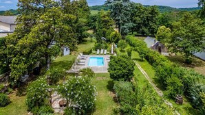 Vista aérea de un jardín exuberante y verde con piscina, rodeado de árboles y un cobertizo pequeño.