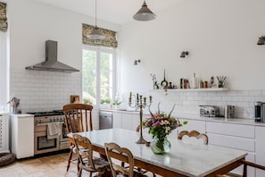 Eine moderne Küche mit weißen Schränken, einem Gasherd, einem eingebauten Backofen und einem Essbereich mit einem Marmortisch und Holzsesseln.