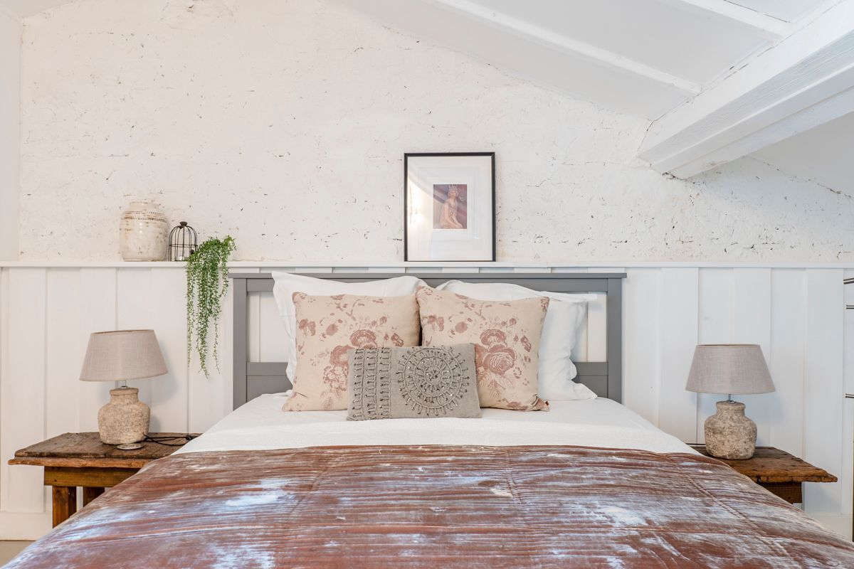 Una camera da letto con un letto, due comodini, un quadro appeso al muro e una pianta sospesa.