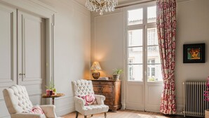 Una habitación con dos sillones tapizados, un aparador de madera, una lámpara de pie y un amplio ventanal con cortinas estampadas.