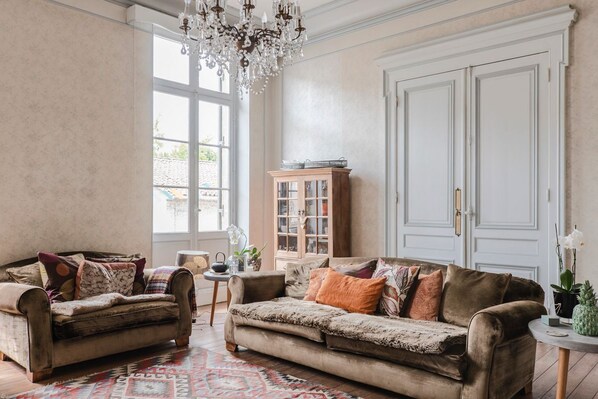 A spacious living room with two sofas, a chandelier, a cabinet, and a large window.