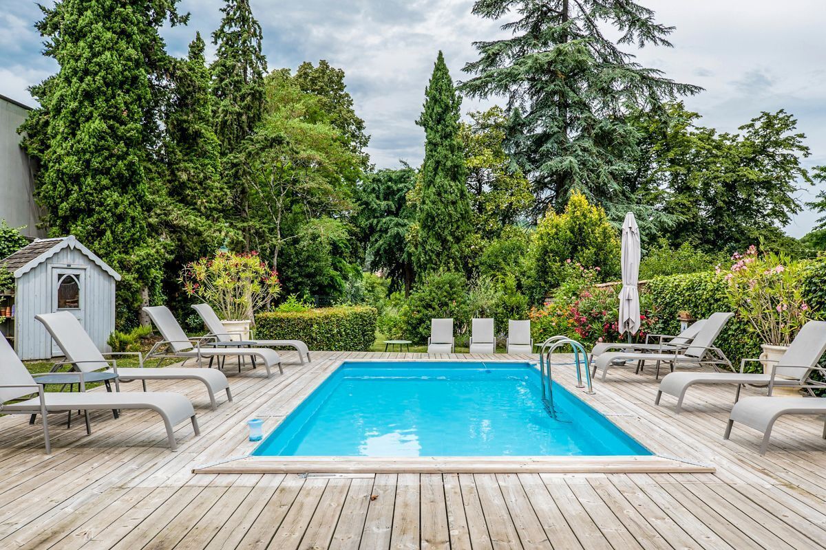 Une piscine rectangulaire dotée d’une terrasse en bois, entourée de chaises longues et d’un petit abri de jardin.