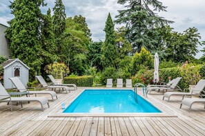 A rectangular pool with a wooden deck, surrounded by lounge chairs and a small shed.