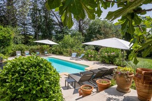 A poolside area with lounge chairs and umbrellas, surrounded by lush greenery and potted plants.