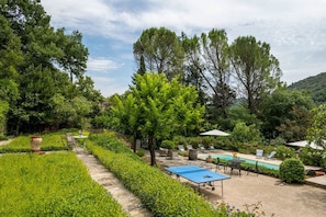 Un jardín con piscina, sillas de descanso y una mesa de ping pong.