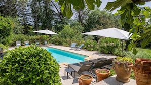 A poolside area with lounge chairs and umbrellas, surrounded by lush greenery and potted plants. - Mas Mayeaux - Six Bedroom Villa, Sleeps 12 (Vaison-la-Romaine)