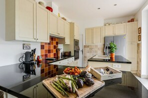 Una cocina moderna con armarios de colores claros, encimera negra y una variedad de verduras frescas sobre la encimera.
