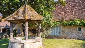 Un bâtiment en pierre avec un toit en tuiles, un puits en pierre et un kiosque en bois.