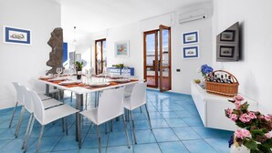 Comedor con una mesa blanca para cuatro personas, sillas blancas, una escultura de piedra y cuadros en las paredes.