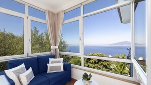 Una habitación con un sofá azul, una mesita blanca y vistas al mar y a la vegetación.