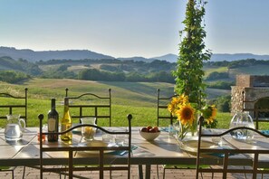 Mesa al aire libre con vistas a colinas onduladas, un jarrón con girasoles y botellas de vino.