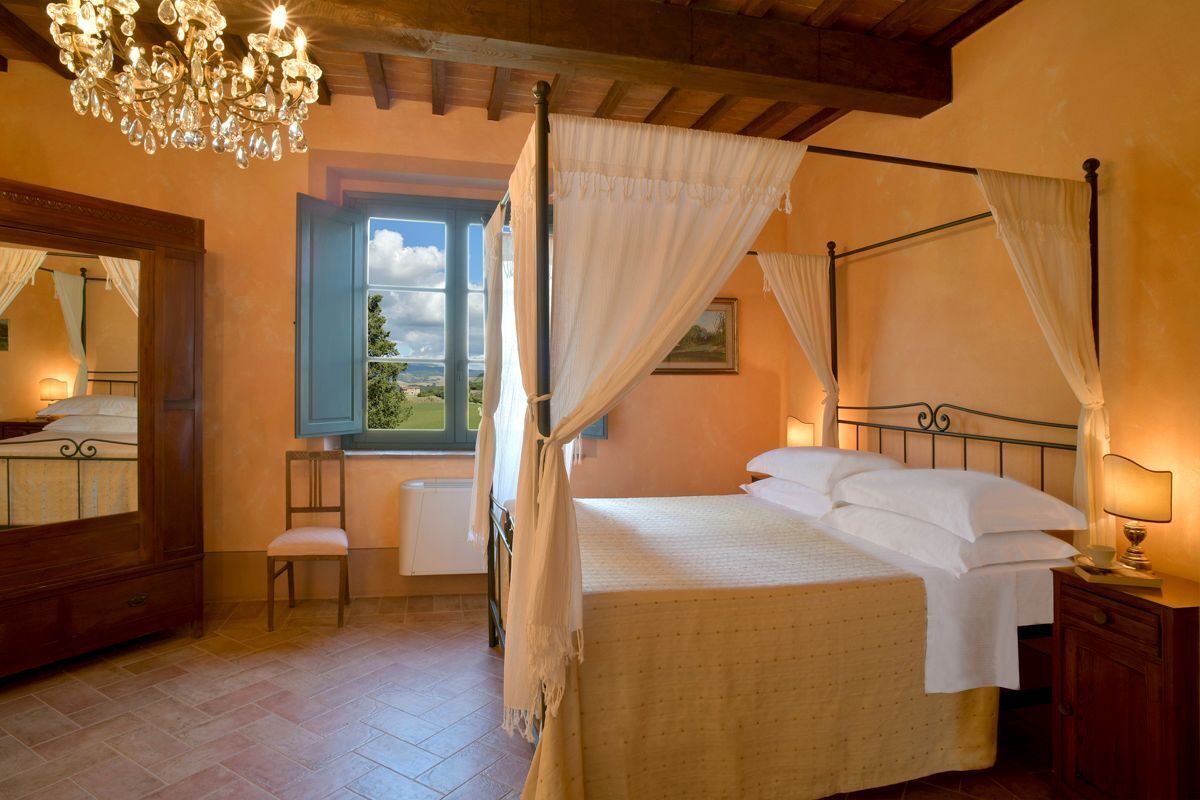 Un lit à baldaquin avec du linge de lit blanc, un lustre et une fenêtre avec des volets bleus.
