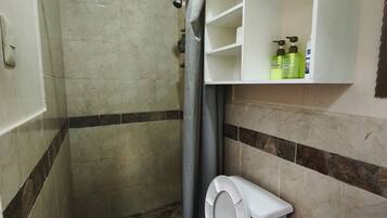 A bathroom with a shower, toilet, and a shelf with toiletries.