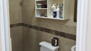 Ein Badezimmer mit Toilette, Dusche und Ablageflächen über der Toilette mit Toilettenartikeln.