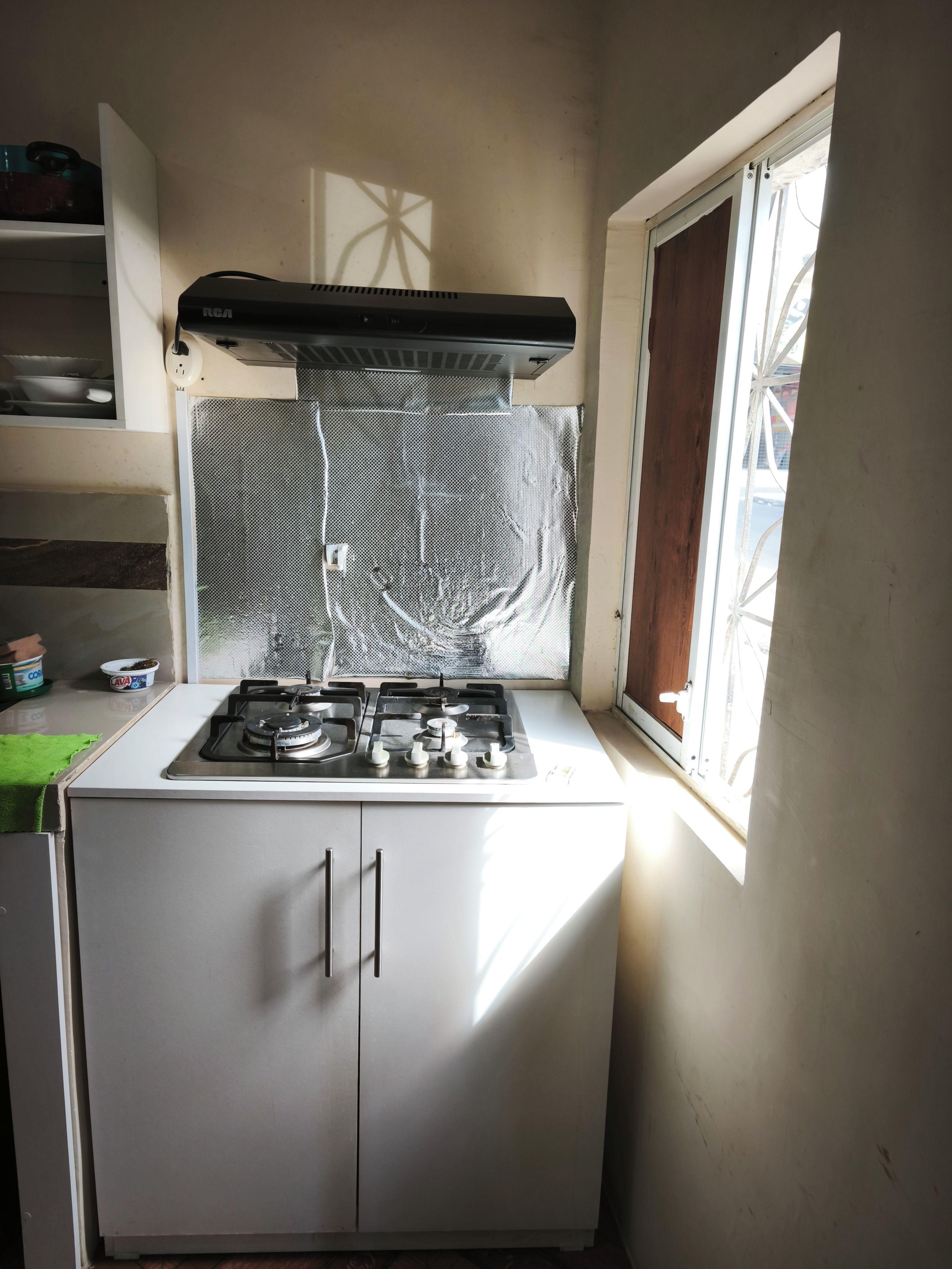 Une cuisine compacte équipée d’une cuisinière à gaz, d’une fenêtre offrant une belle vue et d’une petite étagère où sont rangés des ustensiles de cuisine.