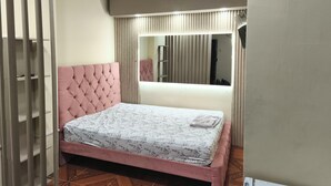 Ein Schlafzimmer mit einem gepolsterten, rosa Kopfstück, einer blumigen Tagesdecke und einem großen Spiegel über dem Bett.