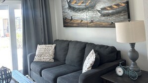 A living room with a grey sofa, a lamp, a clock, and a painting of boats on the wall. - Waterfront Getaway in Charming Beach Town! (Port Charlotte)