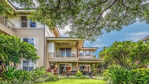 A two-story house with a covered patio, a well-maintained lawn, and various plants. - Hale Laki Stunning Resort Condo, Walk to Beach! (Waikoloa)