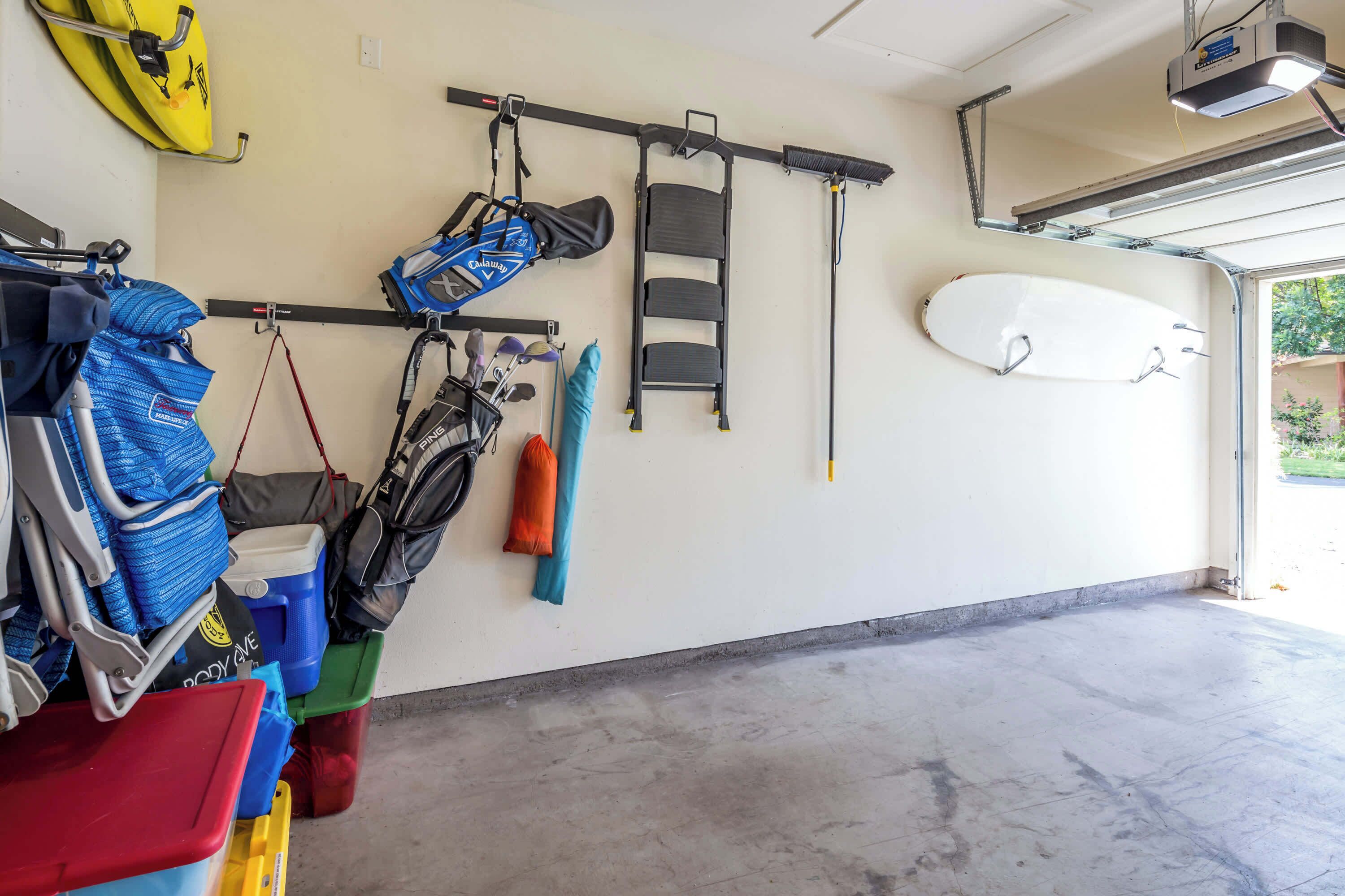A garage with a concrete floor, a ceiling-mounted projector, a kayak, a surfboard, and various bags and containers.