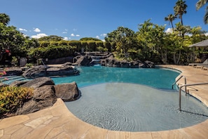 Une piscine à l’eau claire, entourée de rochers et de plantes tropicales.