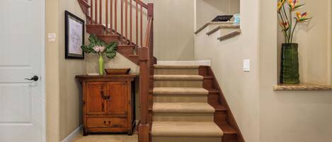 A staircase with a wooden handrail and beige carpeted steps leading to an upper floor.