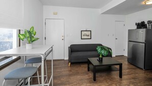 A modern living room with a sofa, a dining table with chairs, a refrigerator, and a potted plant. - Northside Suites (Cincinnati)