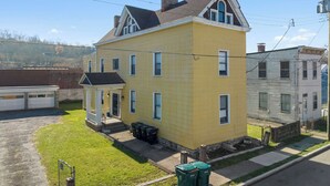 A yellow two-story house with a front porch, a garage, and a small front yard. - Northside Suites (Cincinnati)