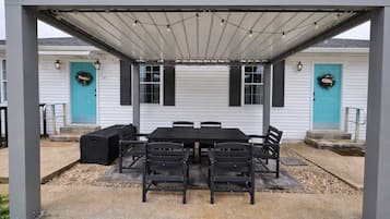 An outdoor patio with a covered table and chairs, surrounded by white walls and blue doors.