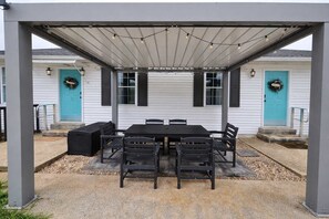 An outdoor patio with a covered table and chairs, surrounded by white walls and blue doors. - Ark Encounter 5 Min | 4BR Family Stay | Sleeps 12 (Williamstown)